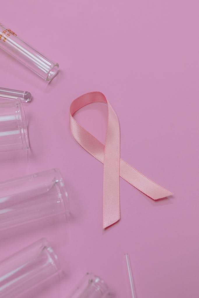Pink ribbon symbolizing cancer awareness on pink background with glass tubes.