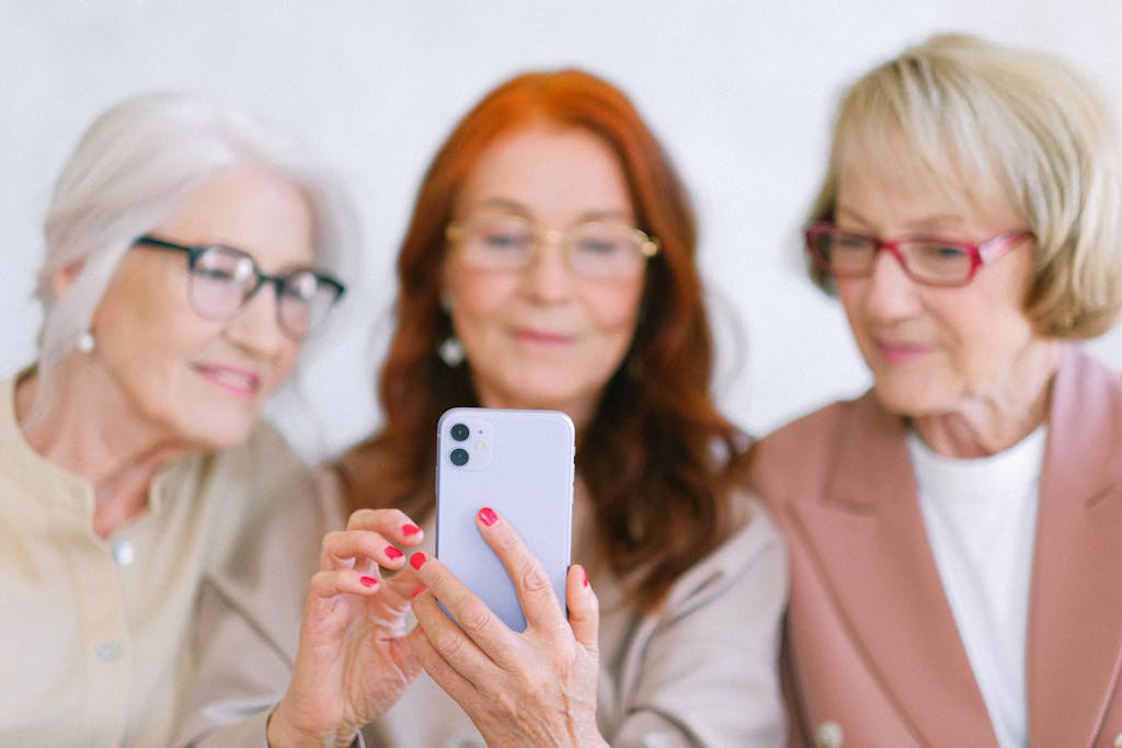Three senior women using a smartphone indoors, sharing a joyful moment together.